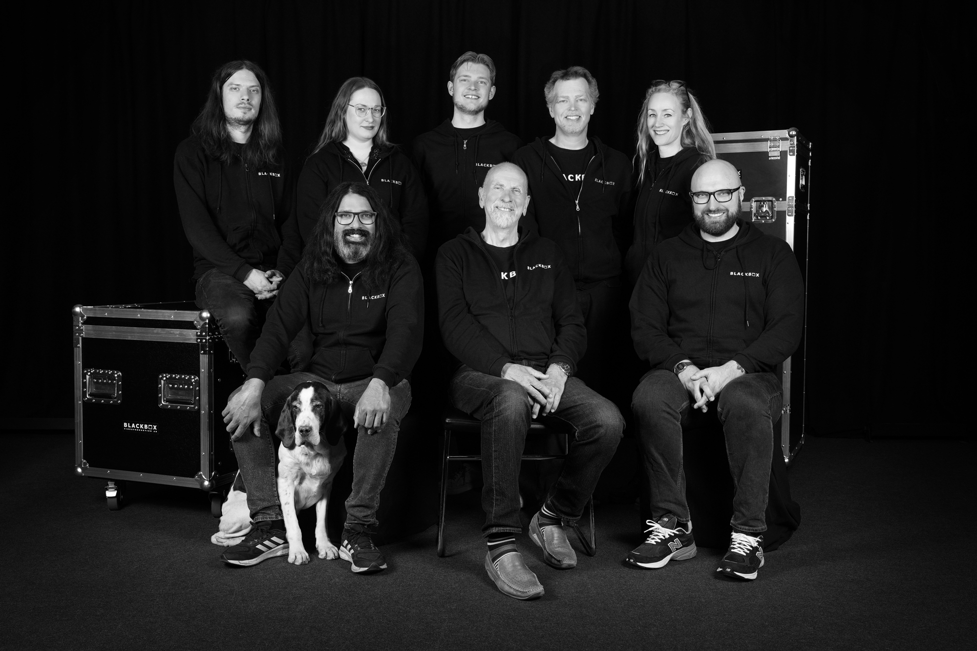Svartvit gruppbild på 8 blackboxanställda samt studiohunden.